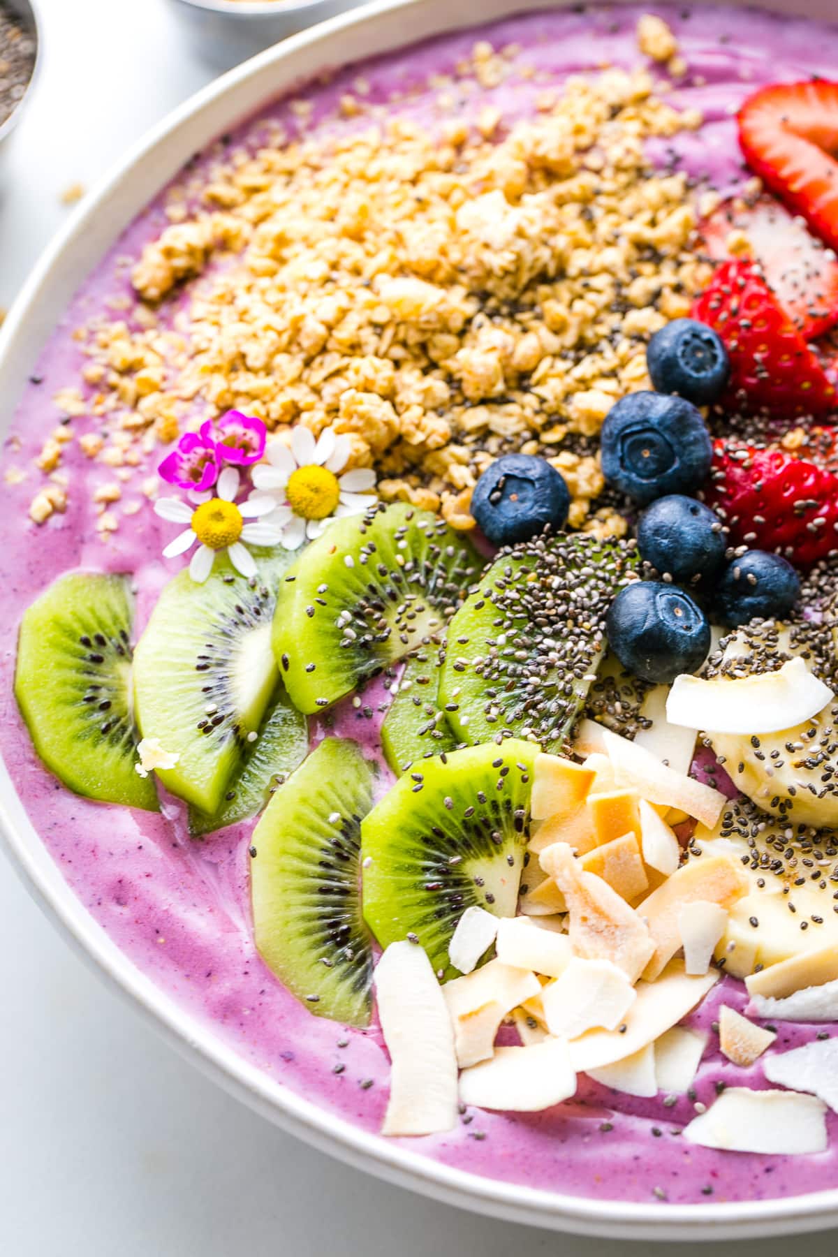 side angle view of healthy smoothie bowl with variety of toppings and items surrounding.