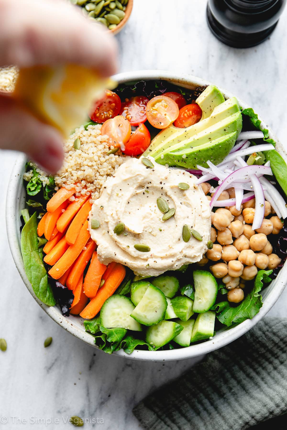 top down view of hummus salad bowl with lemon being squeezed over top with items surrounding.