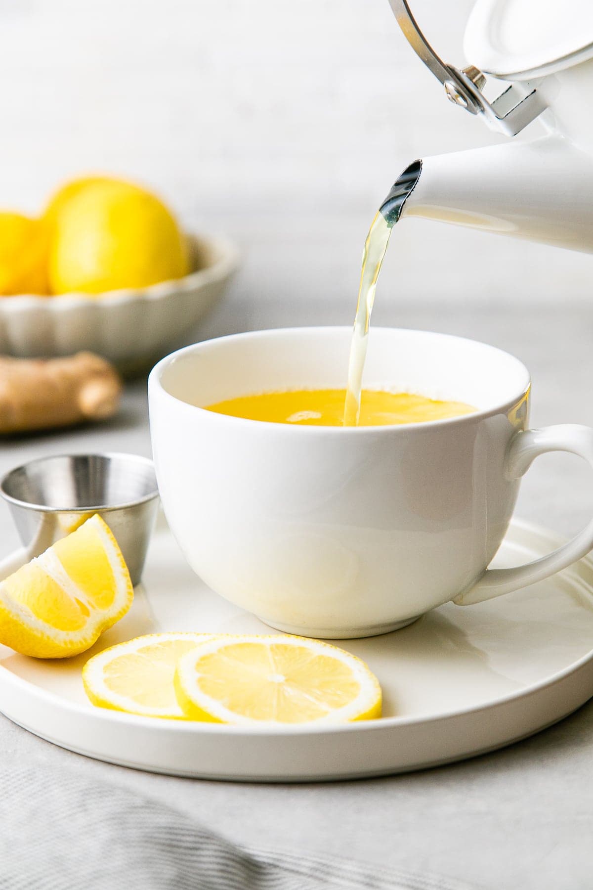 head on view of kettle pouring lemon ginger detox tea with items surrounding.