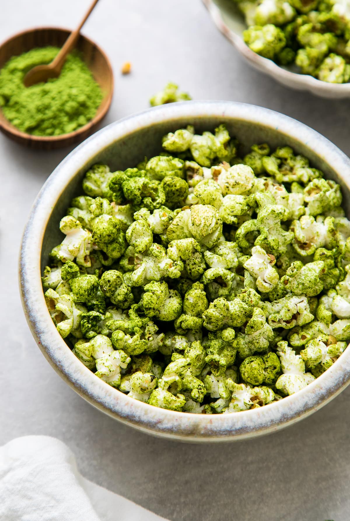 side angle view of serving bowl with green matcha stovetop popcorn with items surrounding.