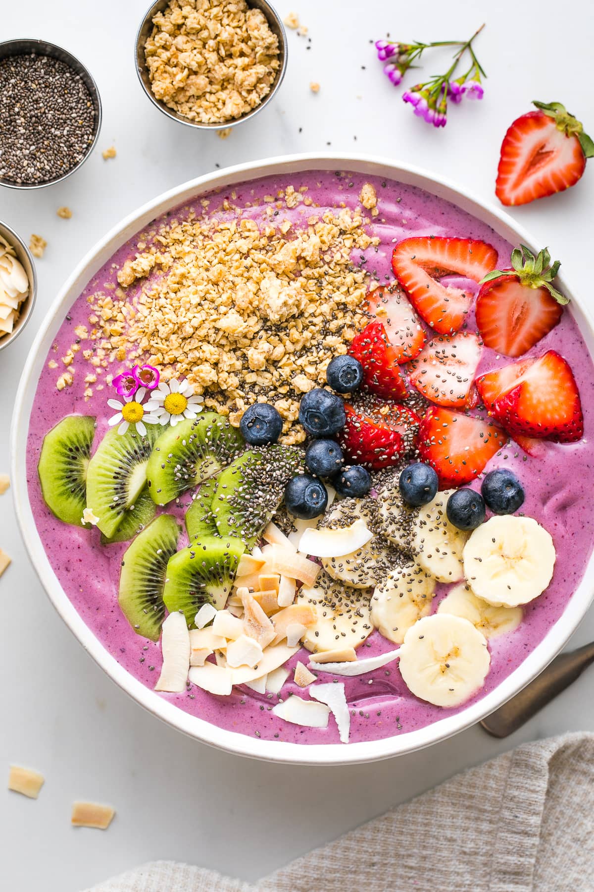 top down view of healthy smoothie bowl with variety of toppings and items surrounding.