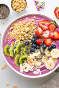 top down view of healthy smoothie bowl with variety of toppings and items surrounding.