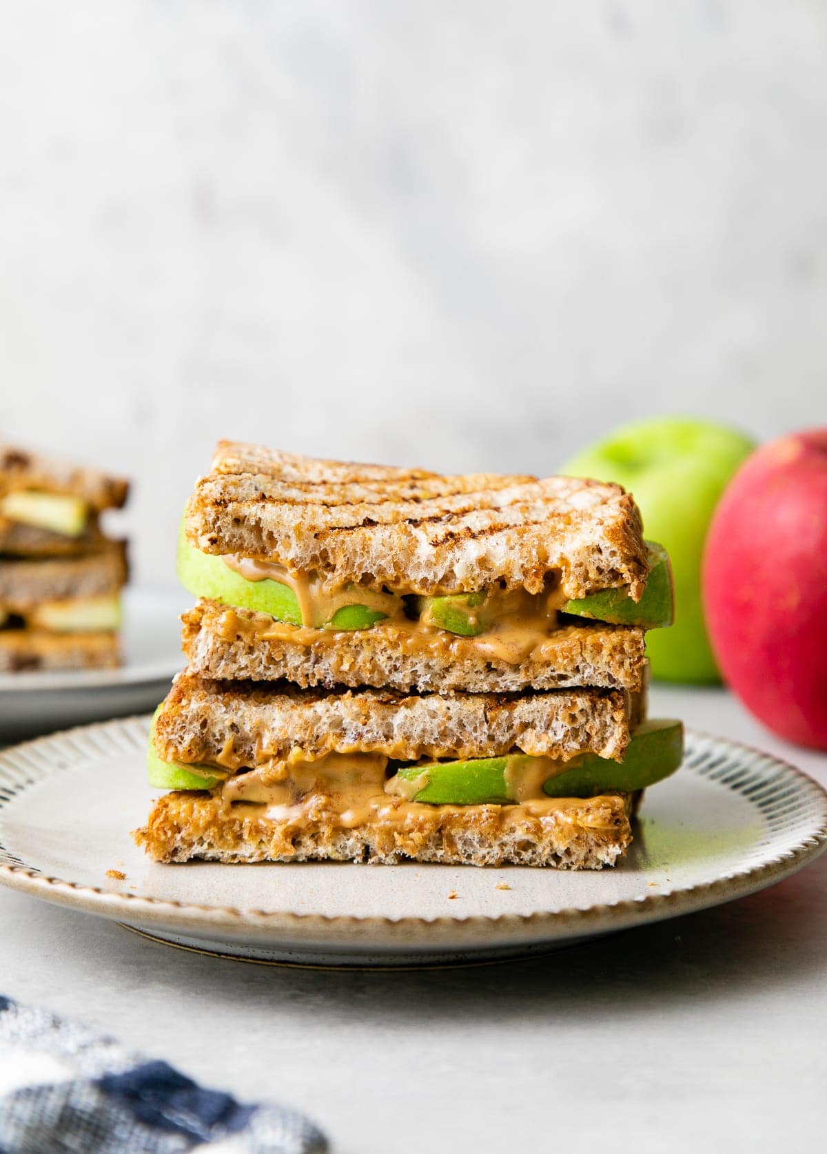 head on view of grilled peanut butter apple sandwich on a plate with items surrounding.