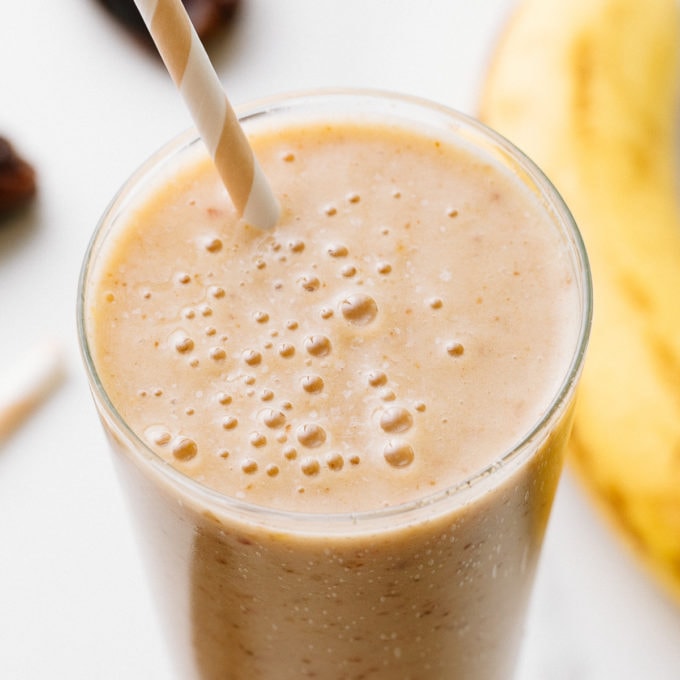 top down view of healthy vanilla date smoothie in a glass with items surrounding.