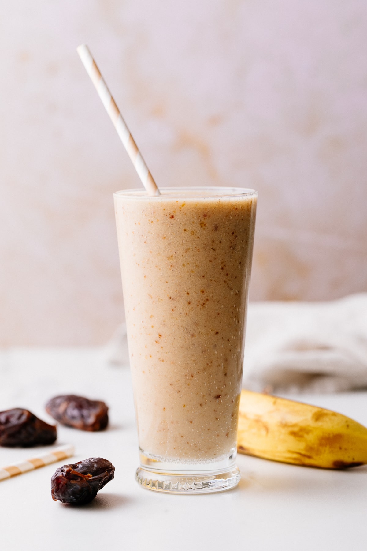 head on view of healthy vanilla date smoothie in a glass with items surrounding.