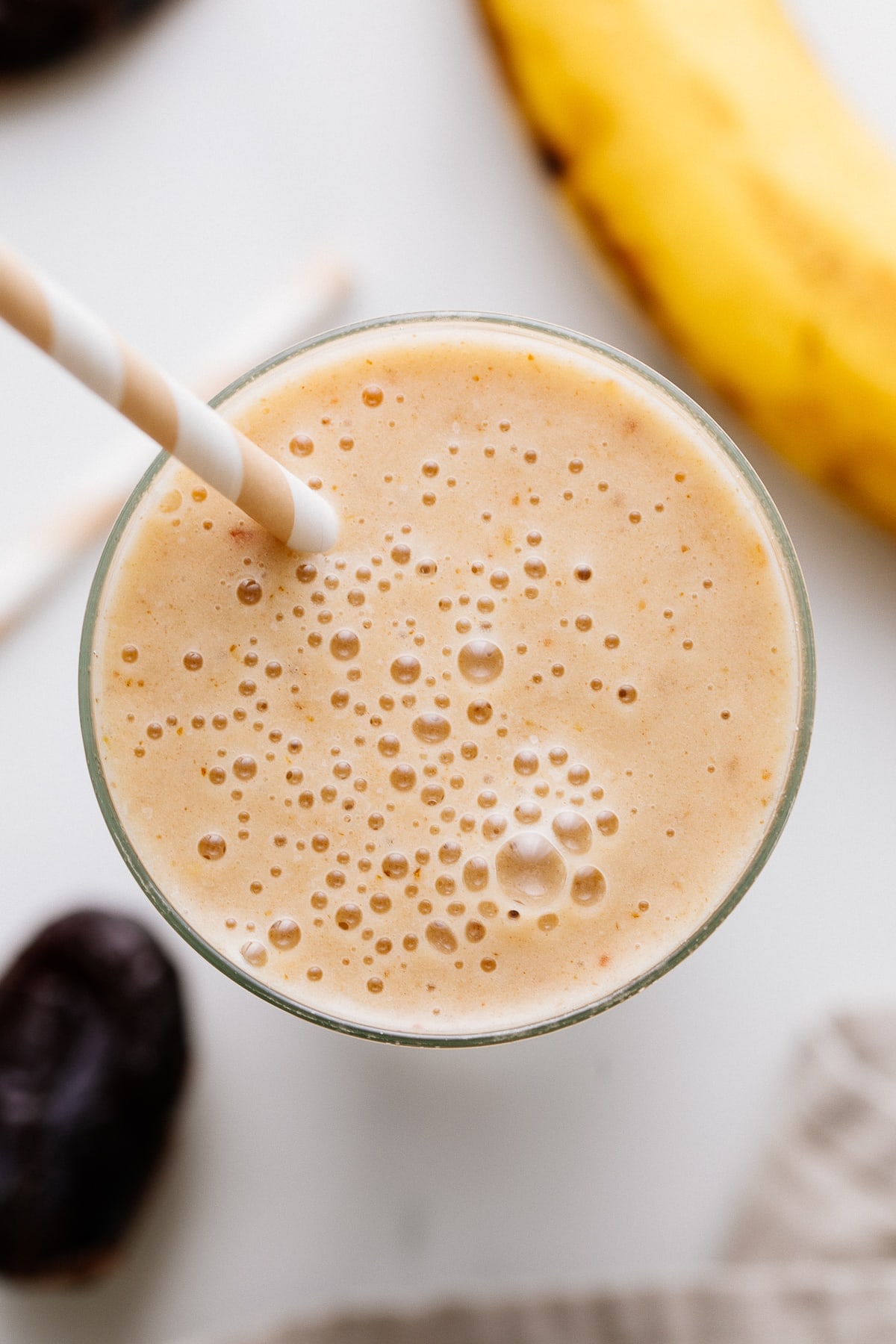 top down view of healthy vanilla date smoothie in a glass with items surrounding.