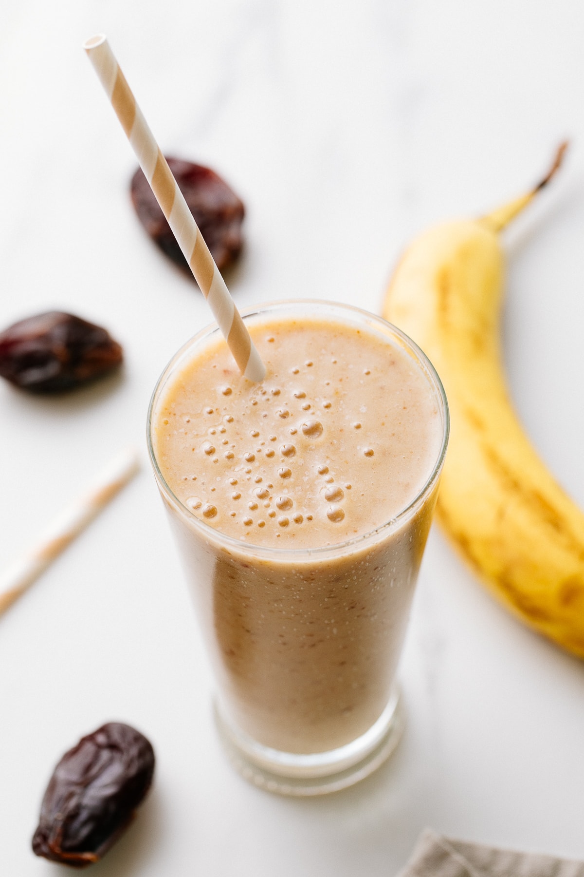 side angle view of healthy vanilla date smoothie in a glass with items surrounding.