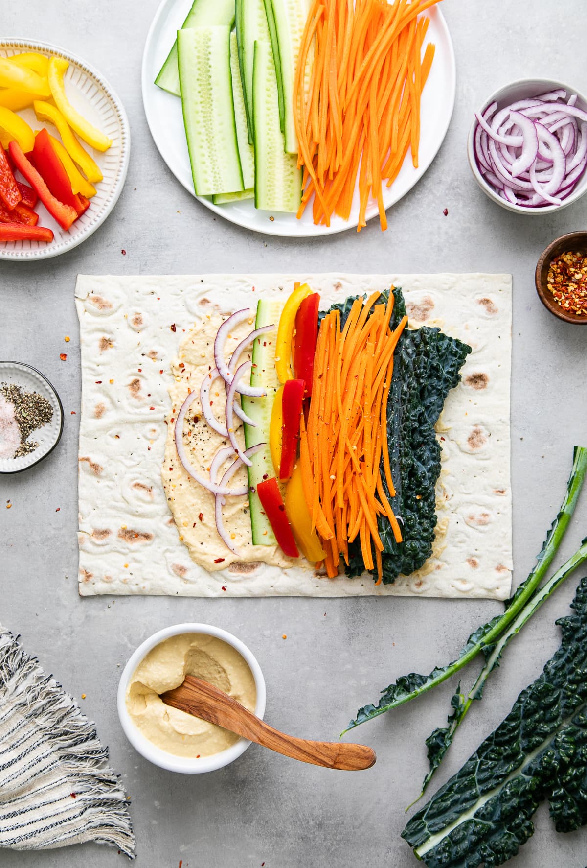top down view showing the process of adding veggies to hummus wrap.