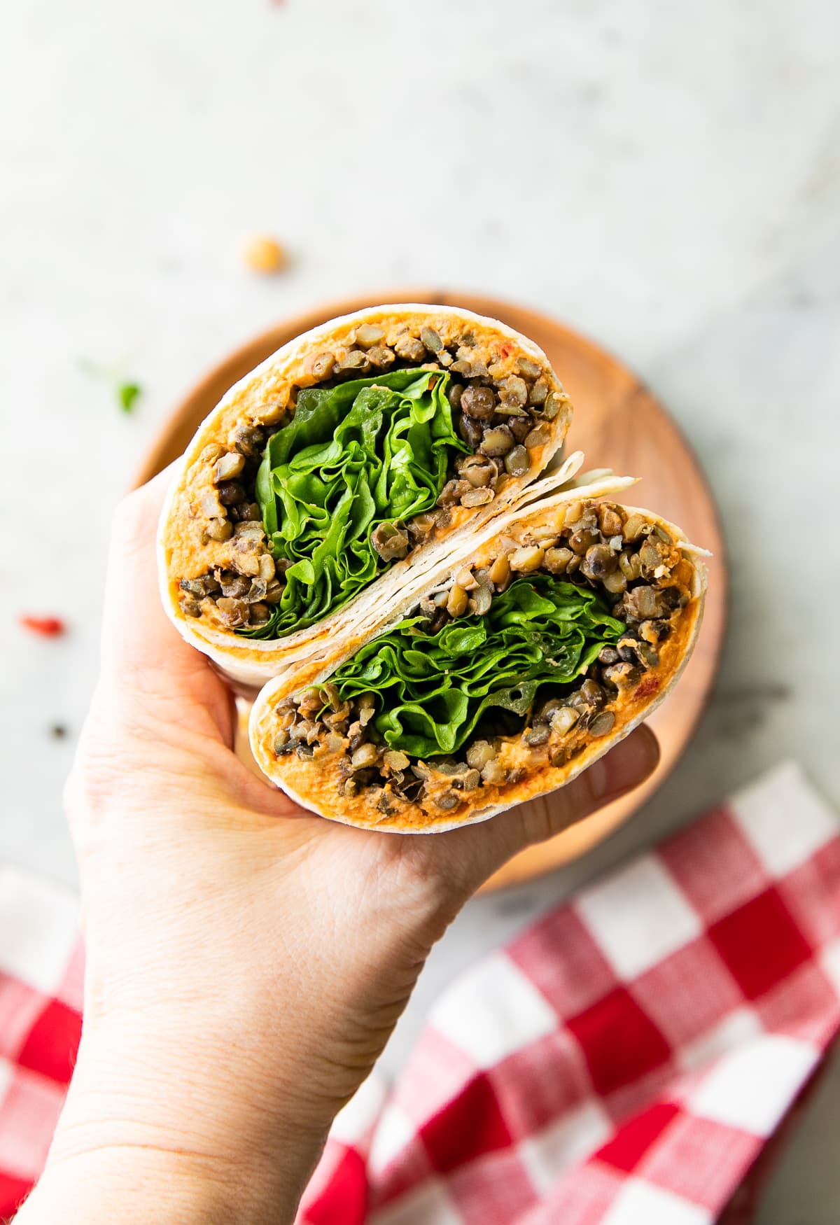 top down view of hand holding two halves of lentil wrap with sun-dried tomatoes hummus.