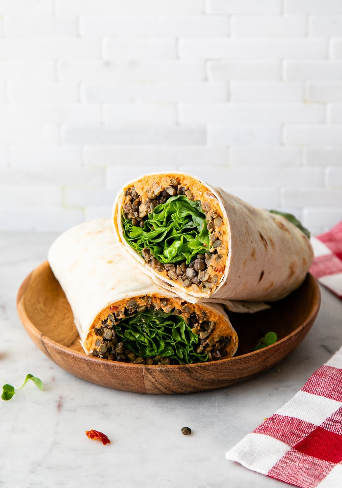 side angle view of two halves of a lentil and sun-dried tomato hummus wrap on a small wooden bowl.