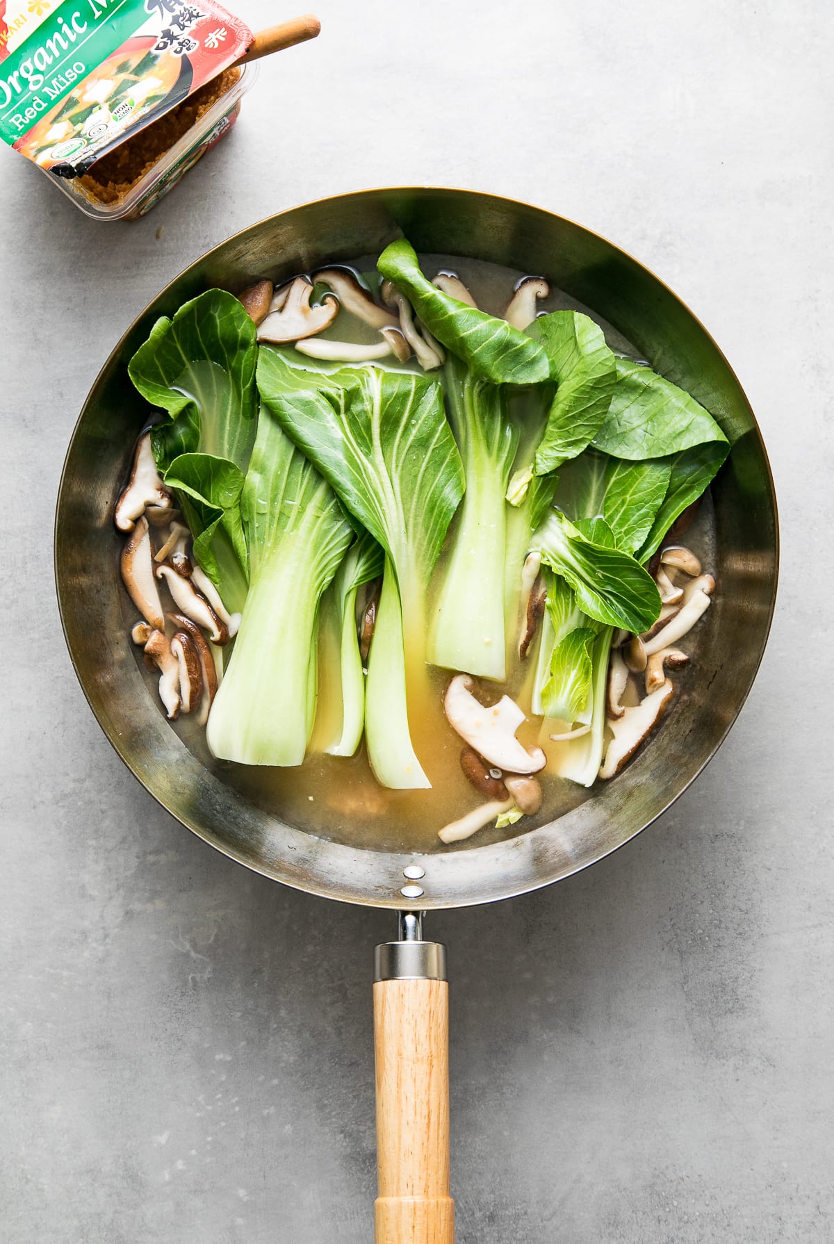 top down view of miso added to wok with mushrooms and bok choy.