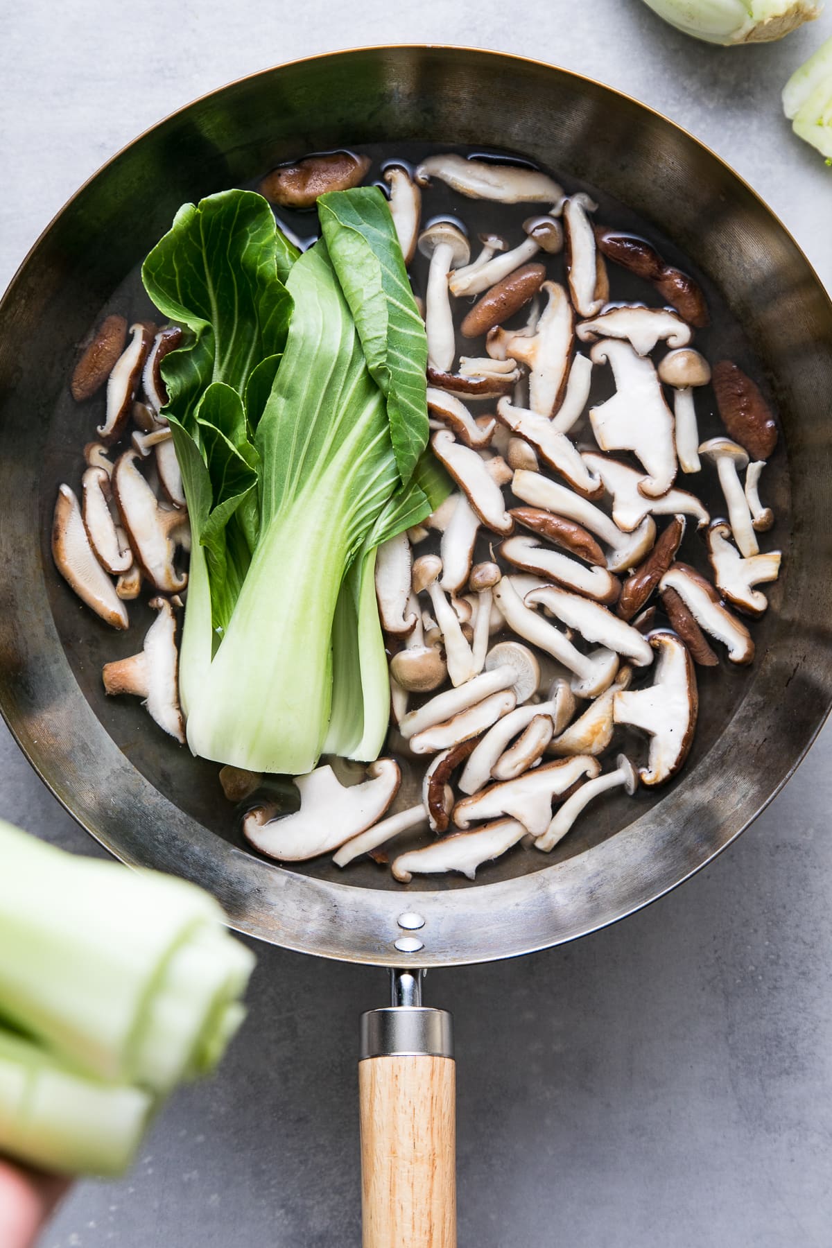 top down view showing the process of adding bok choy to wok for soba noodle soup.