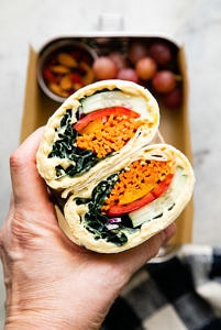 top down view of hand holding a hummus veggie wrap sliced in half.