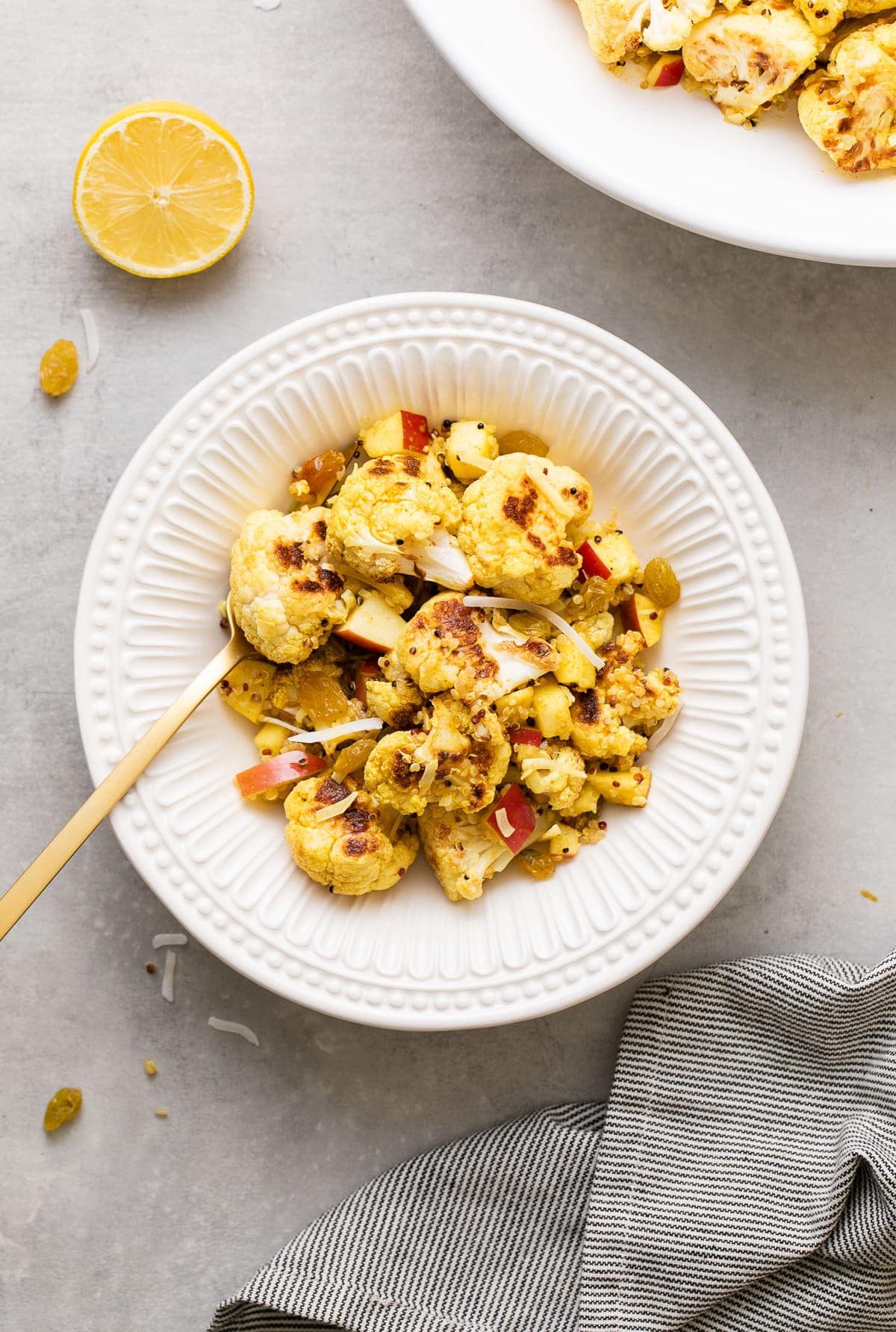 top down view of curried cauliflower salad with quinoa in a white bowl with items surrounding.