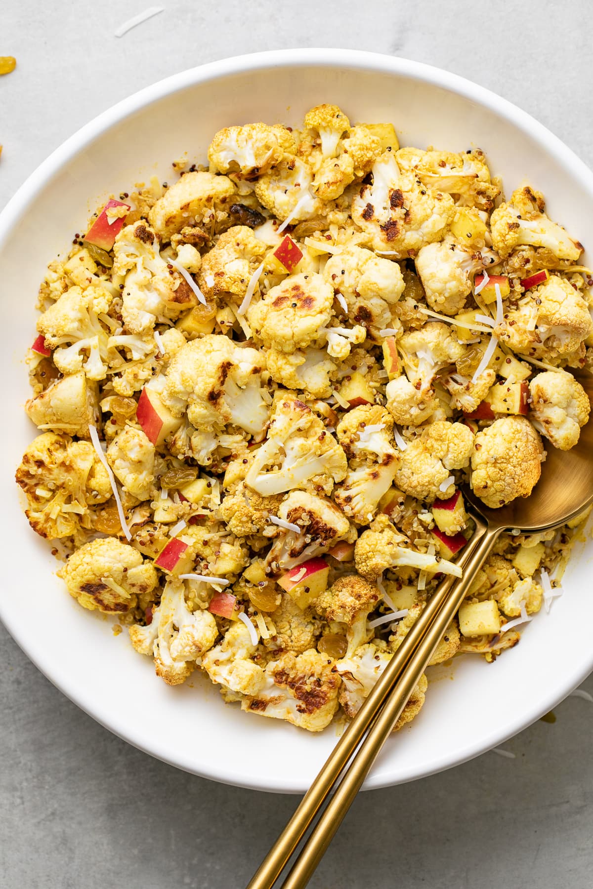 top down view of white serving bowl with healthy curried cauliflower salad with gold serving utensils.