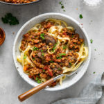 top down view of a bowl with pasta topped with mushroom and lentil ragu with fork and items surrounding.