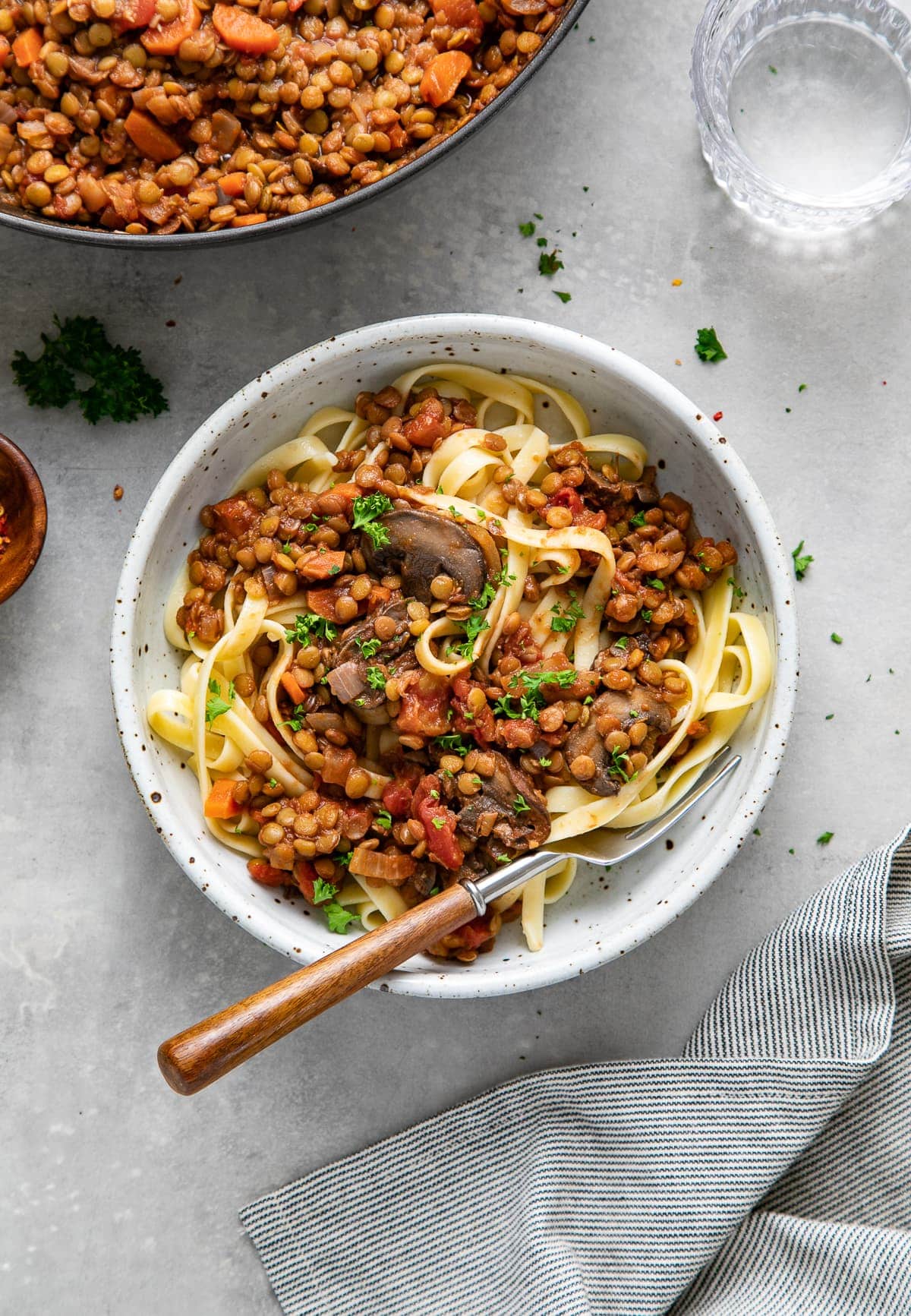 top down view of a bowl with pasta topped with mushroom and lentil ragu with fork and items surrounding.