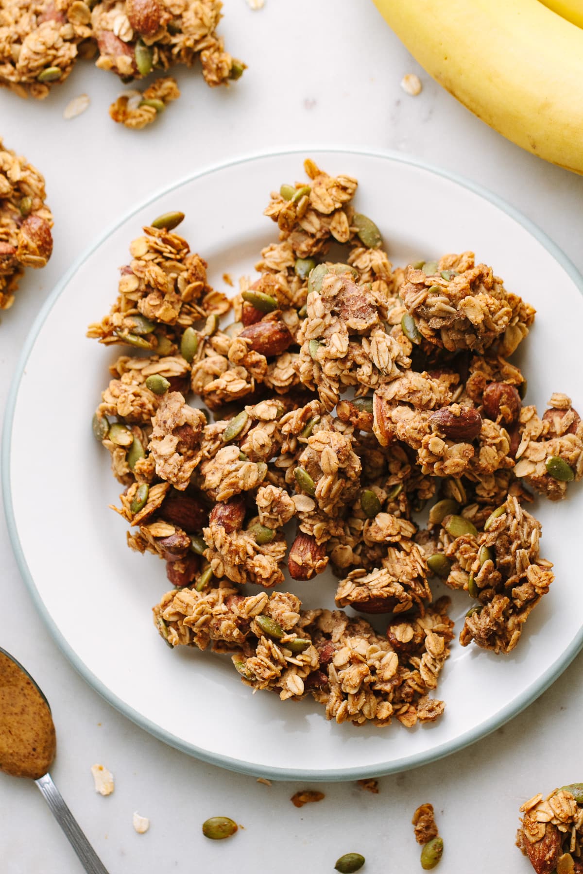 top down view of peanut butter banana granola clusters on a plate, surrounded by items.