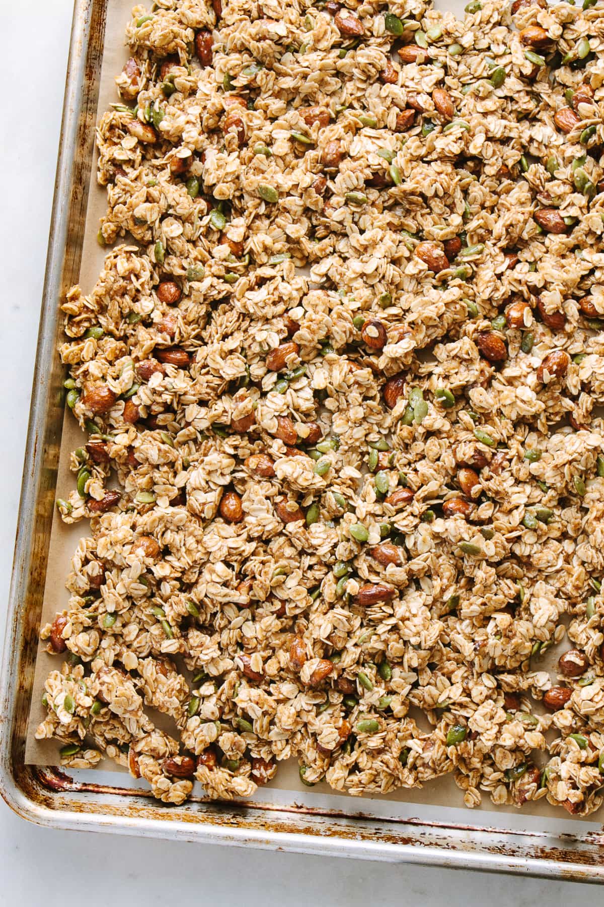 top down view of wet granola spread evenly on a rimmed baking sheet before baking.