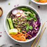 top down view of cold soba noodle bowl with with veggies and miso dressing and items surrounding.