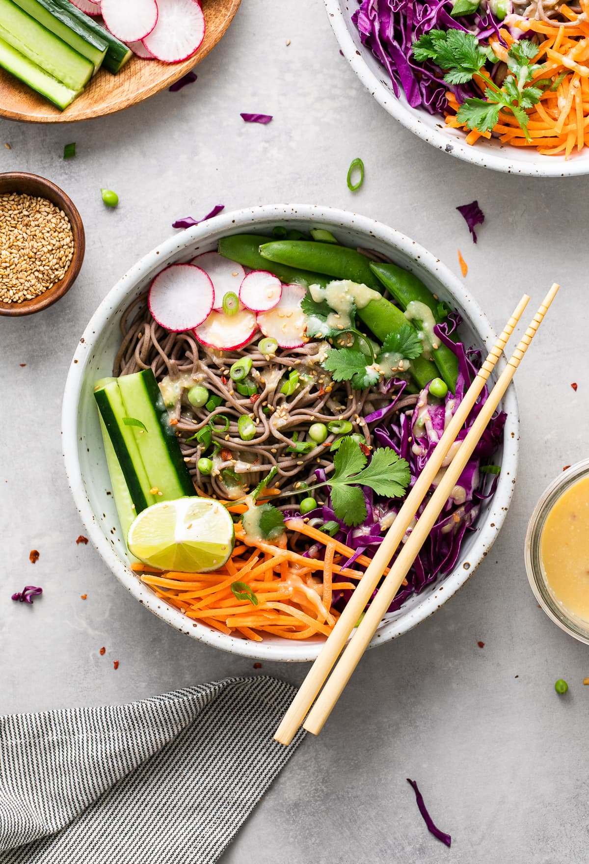 top down view of cold soba noodle bowl with with veggies and miso dressing and items surrounding.
