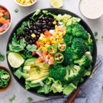 top down view of black bean broccoli salad with avocado in a black bowl with items surrounding.
