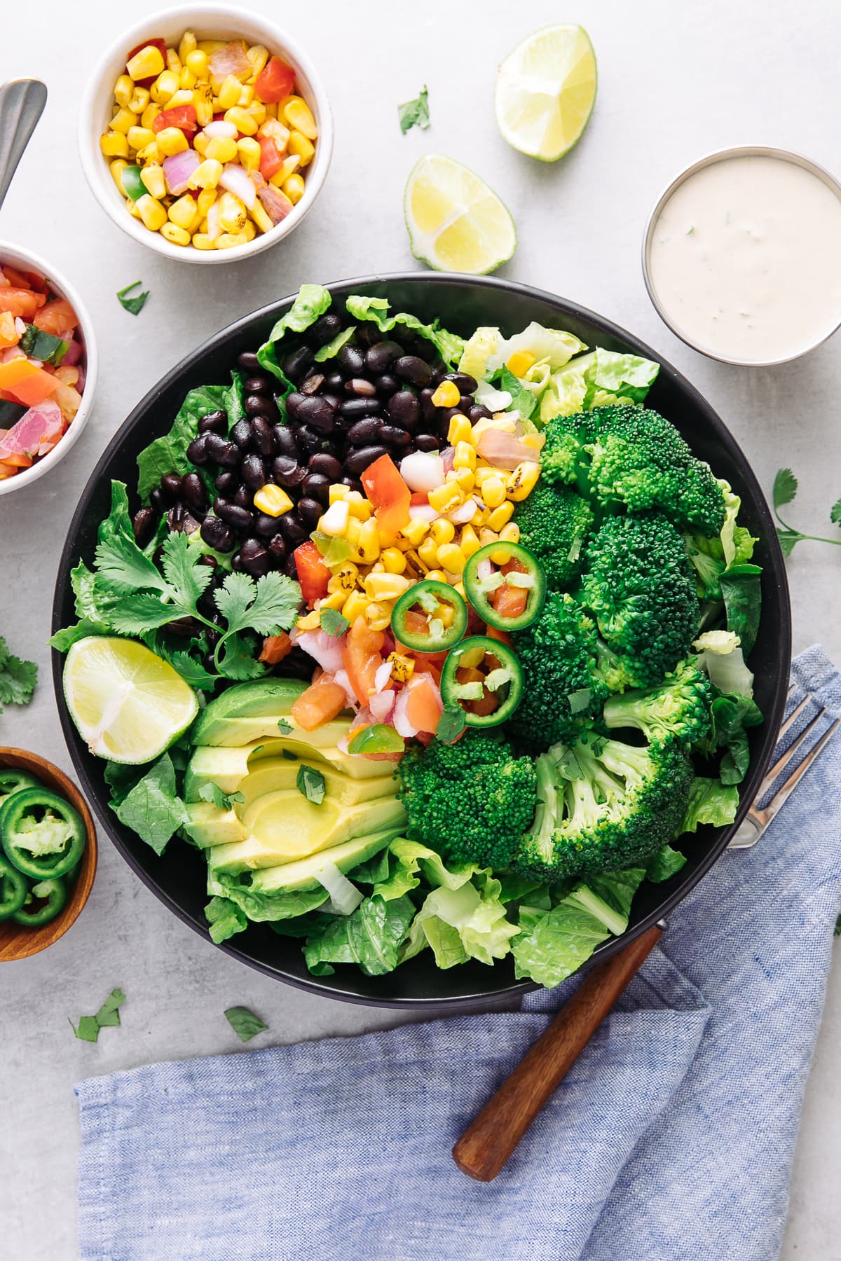 top down view of black bean broccoli salad with avocado in a black bowl with items surrounding.