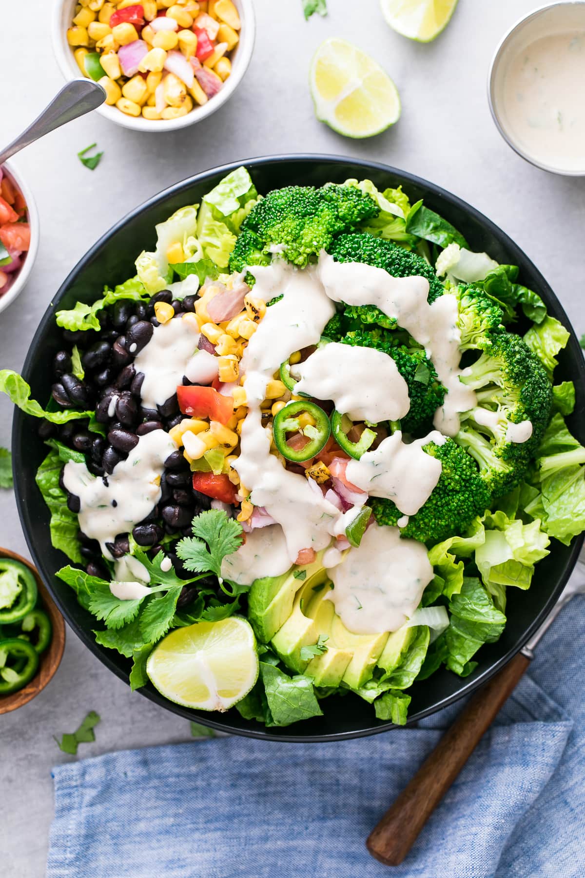 top down view of black bean broccoli salad with avocado and cumin tahini dressing in a black bowl with items surrounding.
