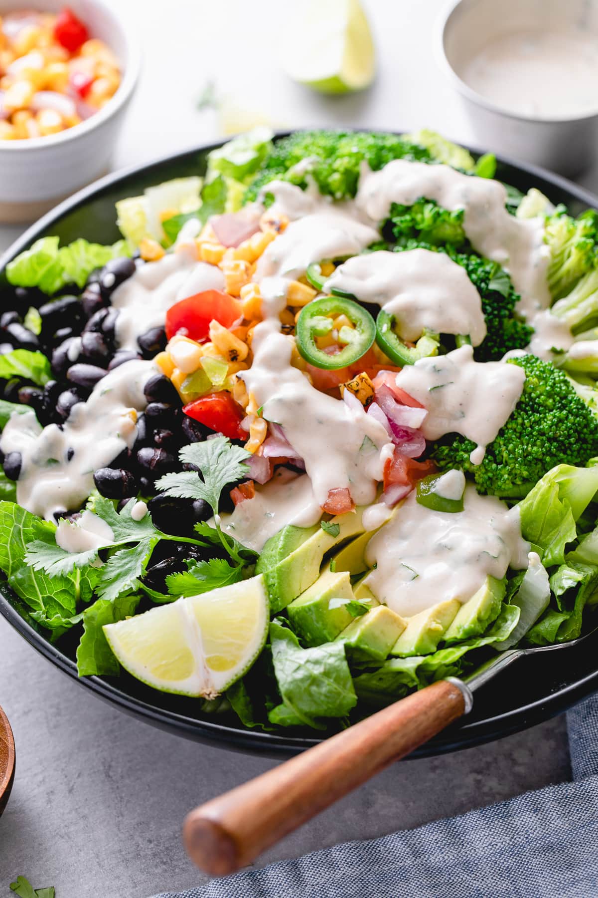 side angle view of black bean broccoli salad with avocado and cumin tahini dressing in a black bowl with items surrounding.