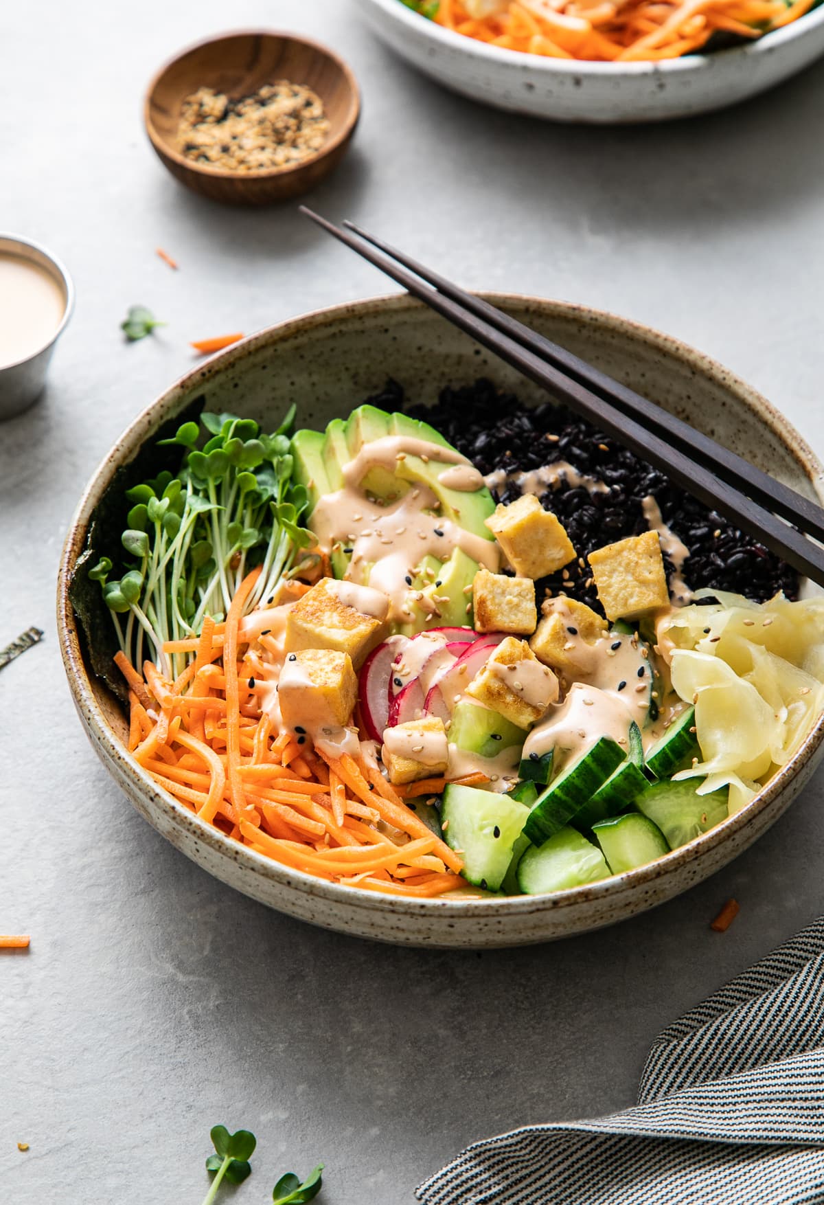 side angle view of vegan sushi bowl topped with creamy dynamite sauce with items surrounding.