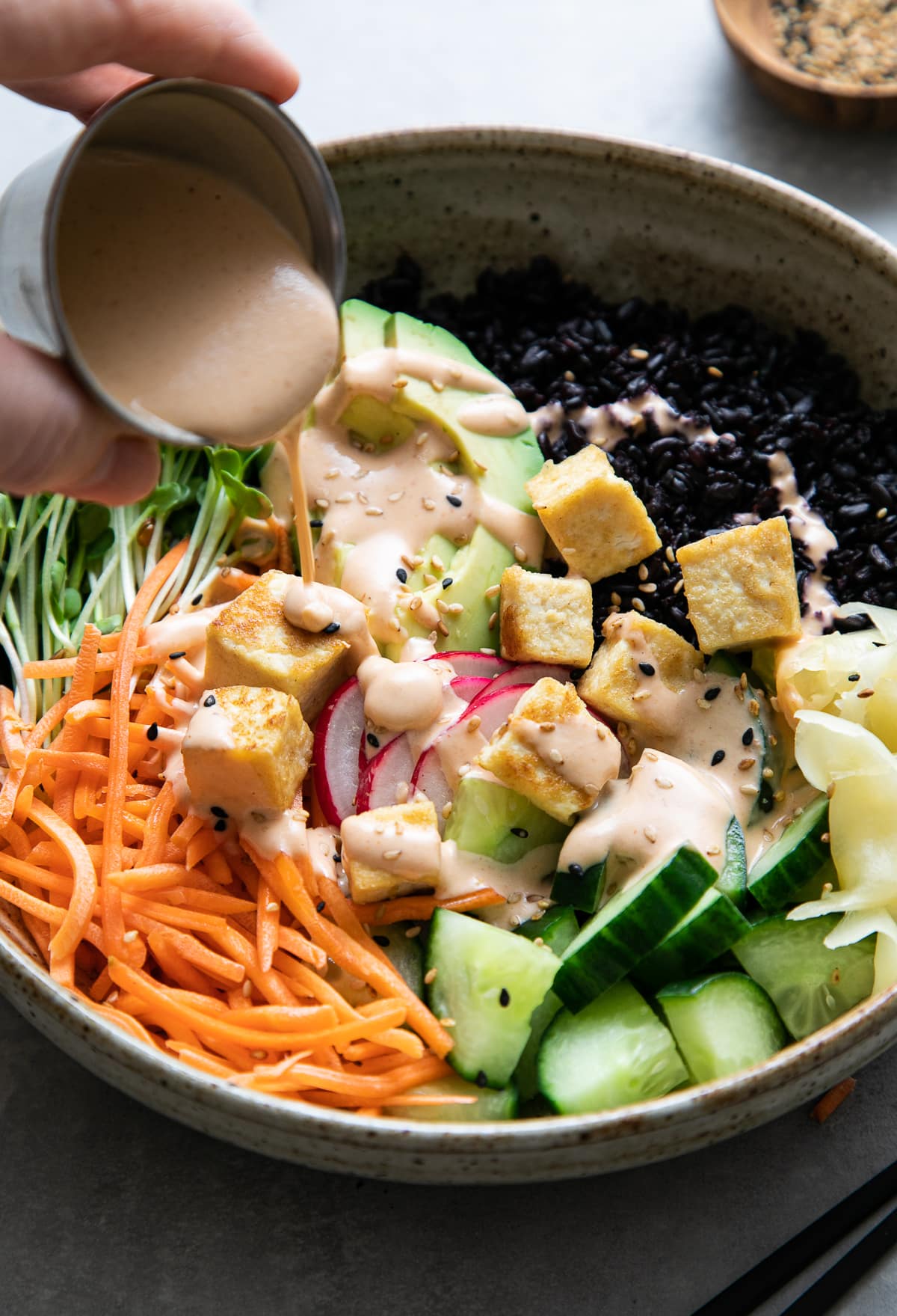 side angle view of creamy dynamite sauce being poured over freshly made sushi bowl.