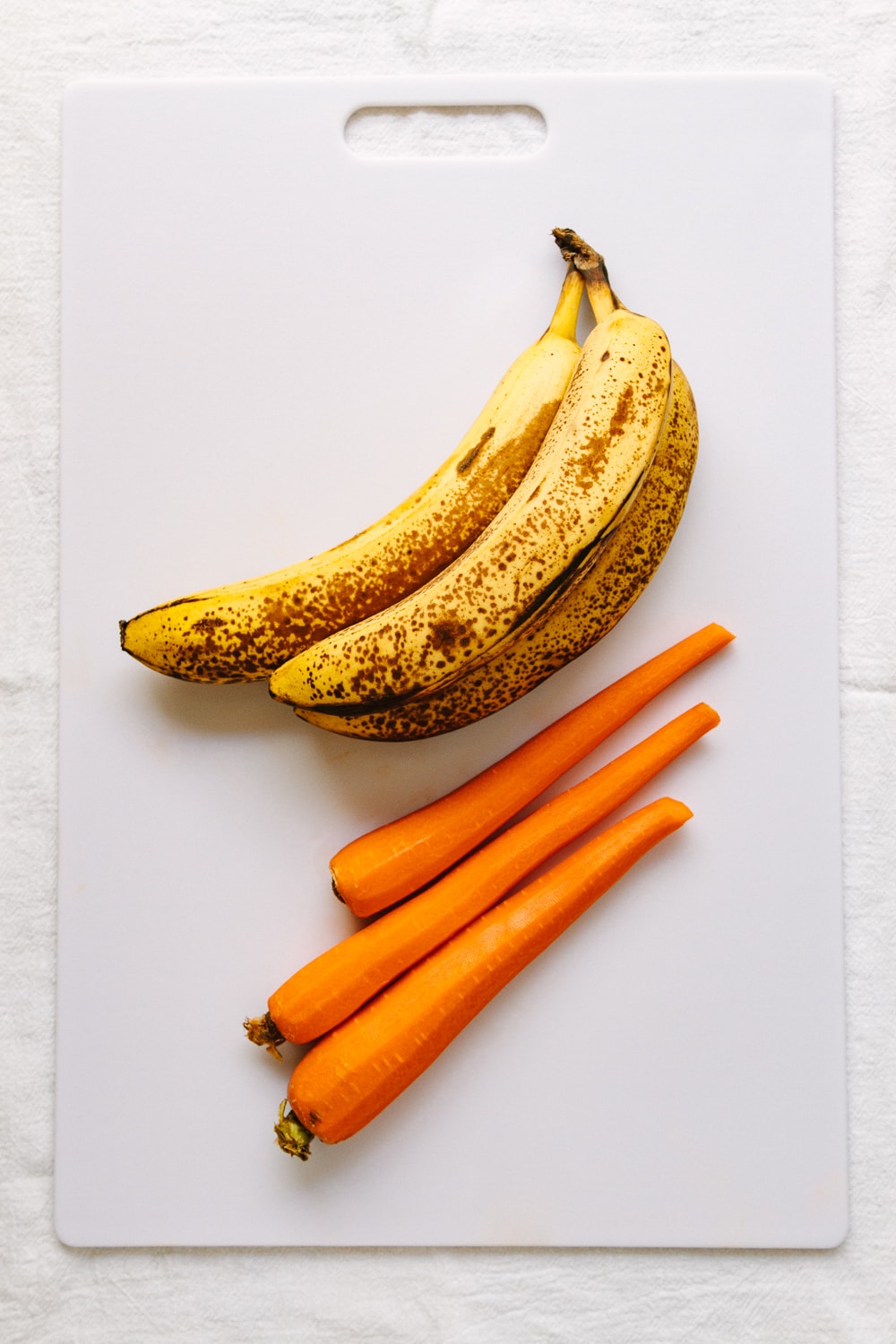 top down view of carrots and bananas on a white cutting board.