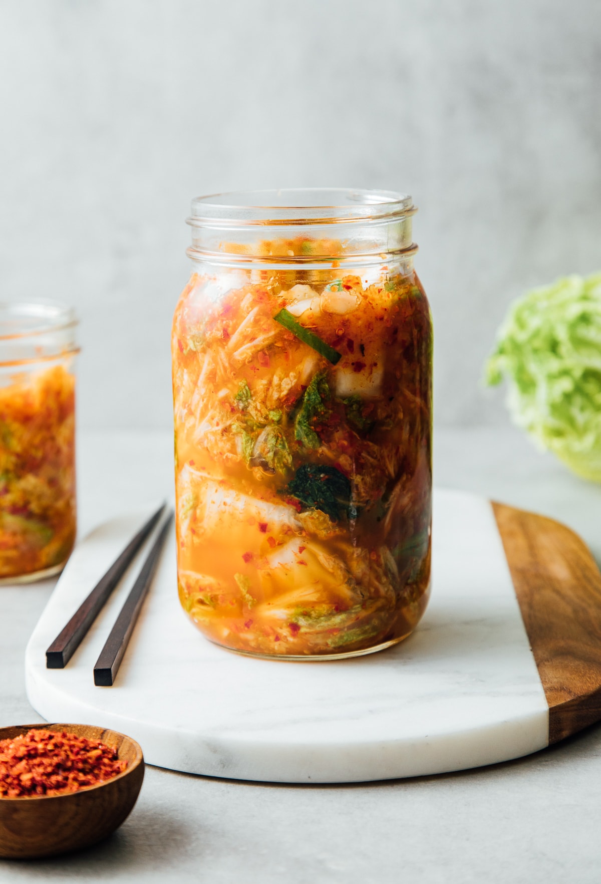 head on view of freshly fermented kimchi added to mason jar with items surrounding.