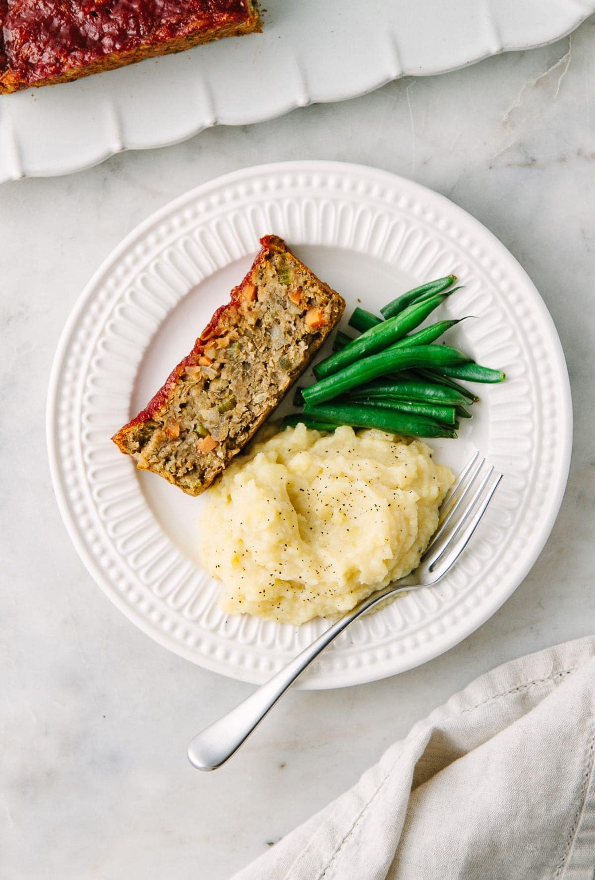 top down view of a serving of vegan lentil loaf with apple, sage and fennel on a white plate with items.