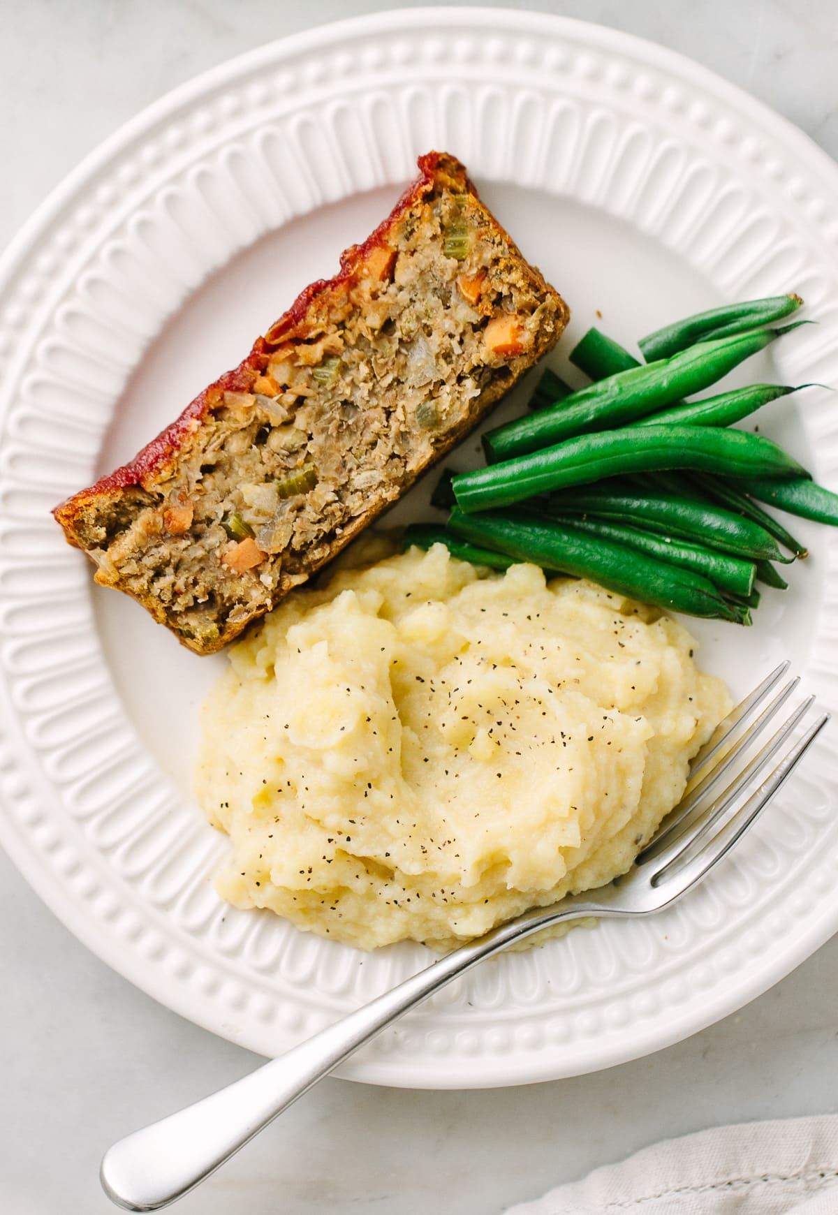 top down view of a serving of vegan lentil loaf with apple, sage and fennel on a white plate with items.