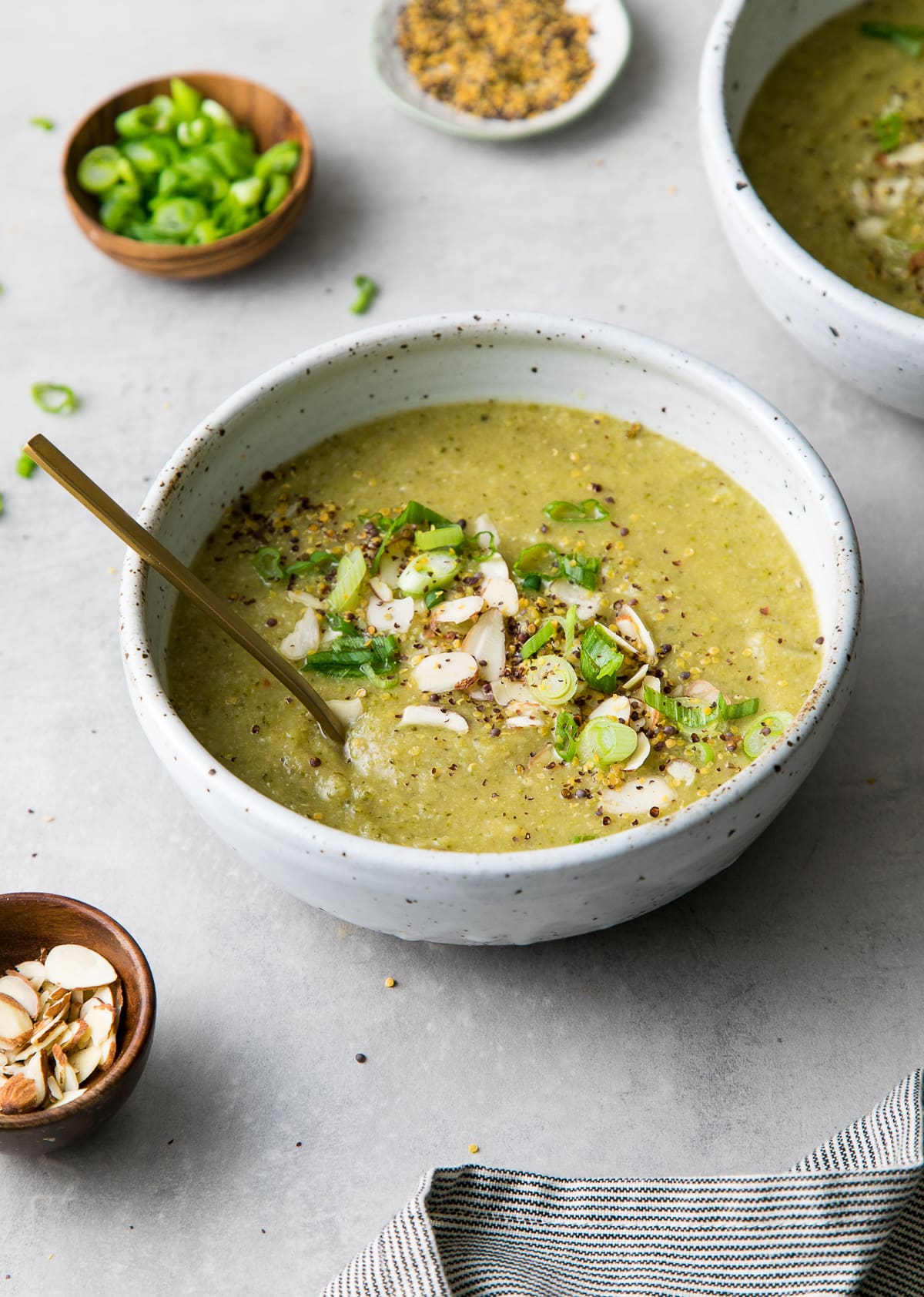 side angle view of bowl of creamy broccoli red lentil soup with spoon and items surrounding.