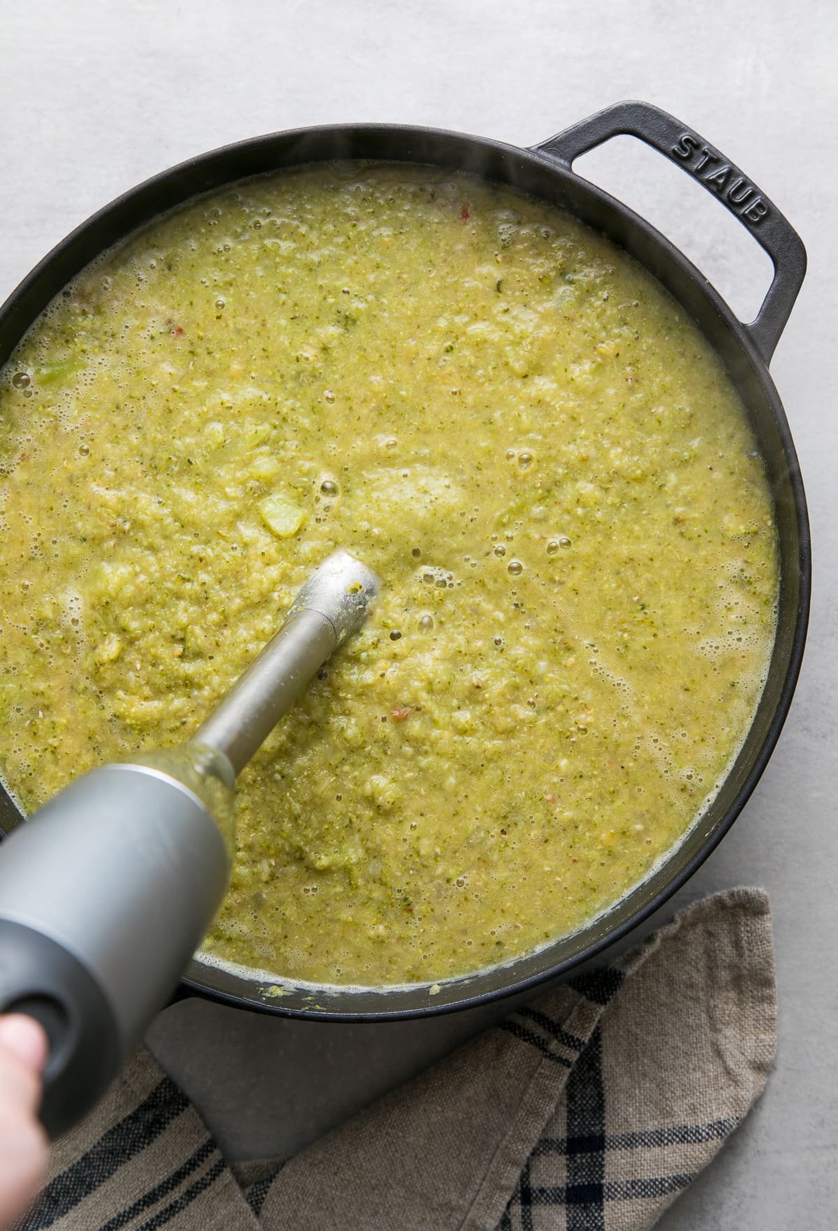 top down view showing the process of pureeing creamy broccoli red lentil soup in black pot.