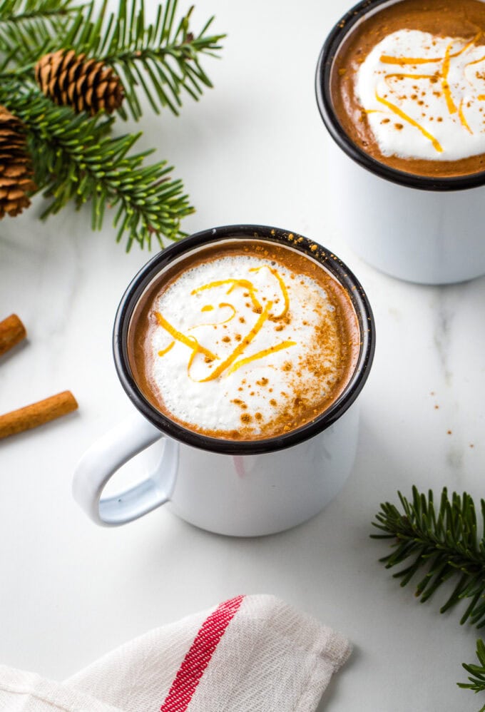 side angle view of orange hot chocolate in a white cup with items surrounding.