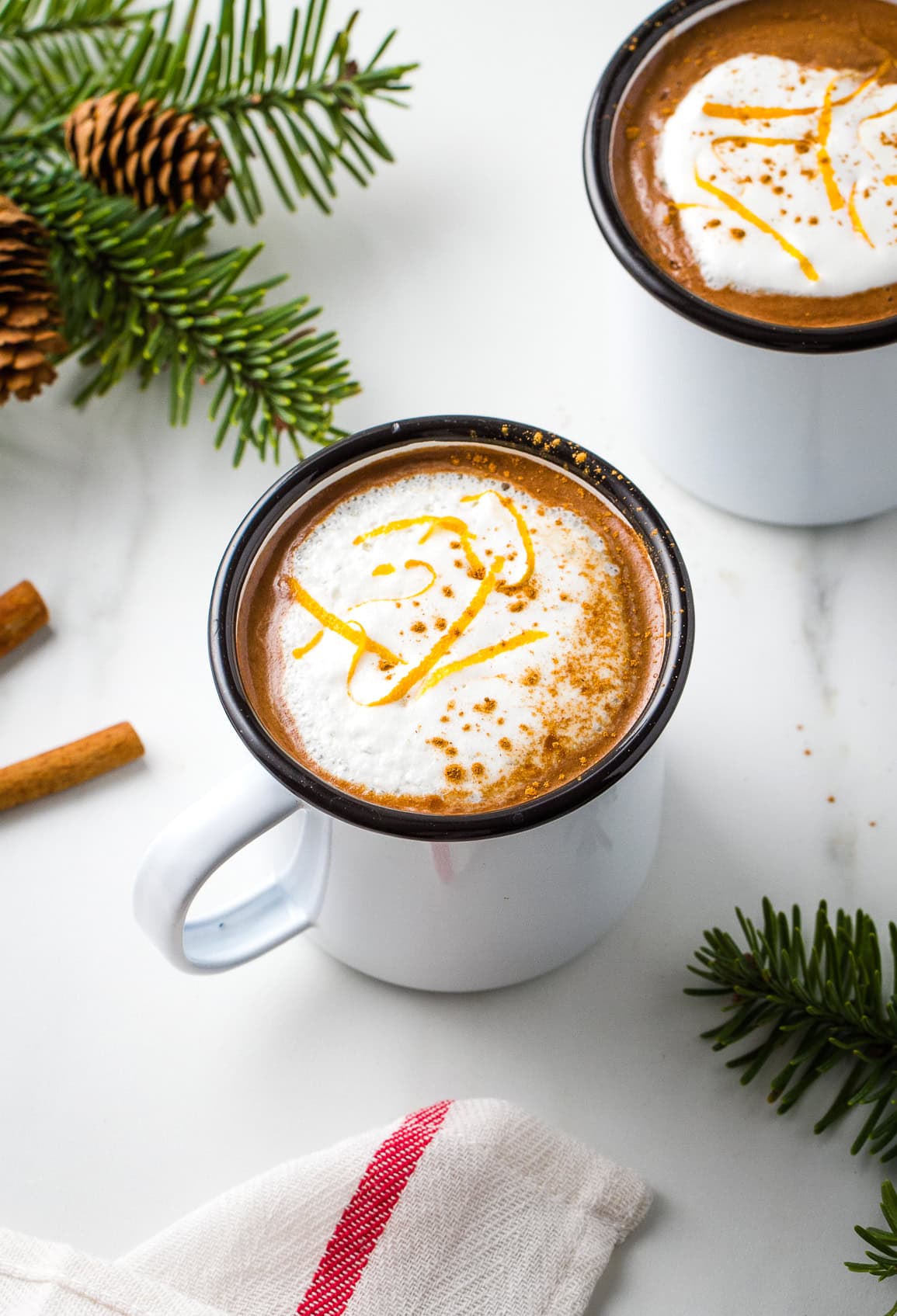 side angle view of orange hot chocolate in a white cup with items surrounding.
