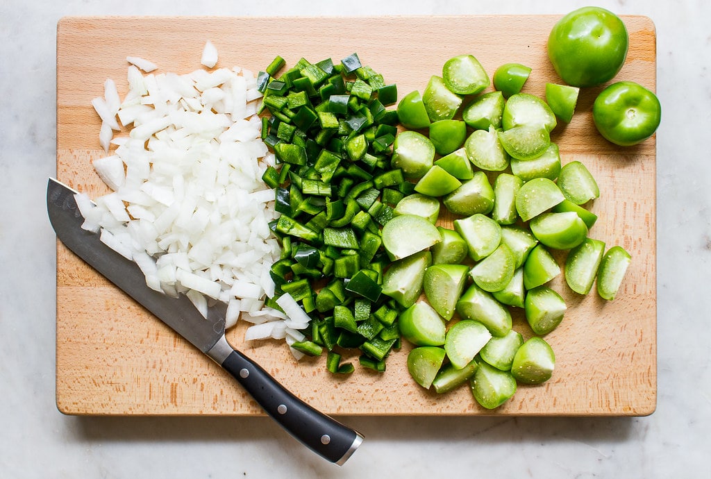 top down view of chopped onion, poblano and tomatillos on a wooden cutting board.