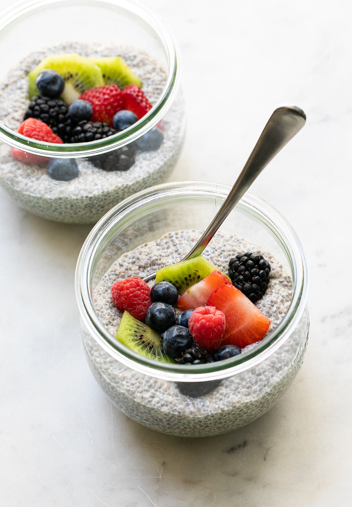 side angle view of glass jar with serving of chia pudding and fresh fruit with spoon.