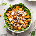 top down view of sweet potato chickpea salad with crispy shallots and tahini dressing with items surrounding.
