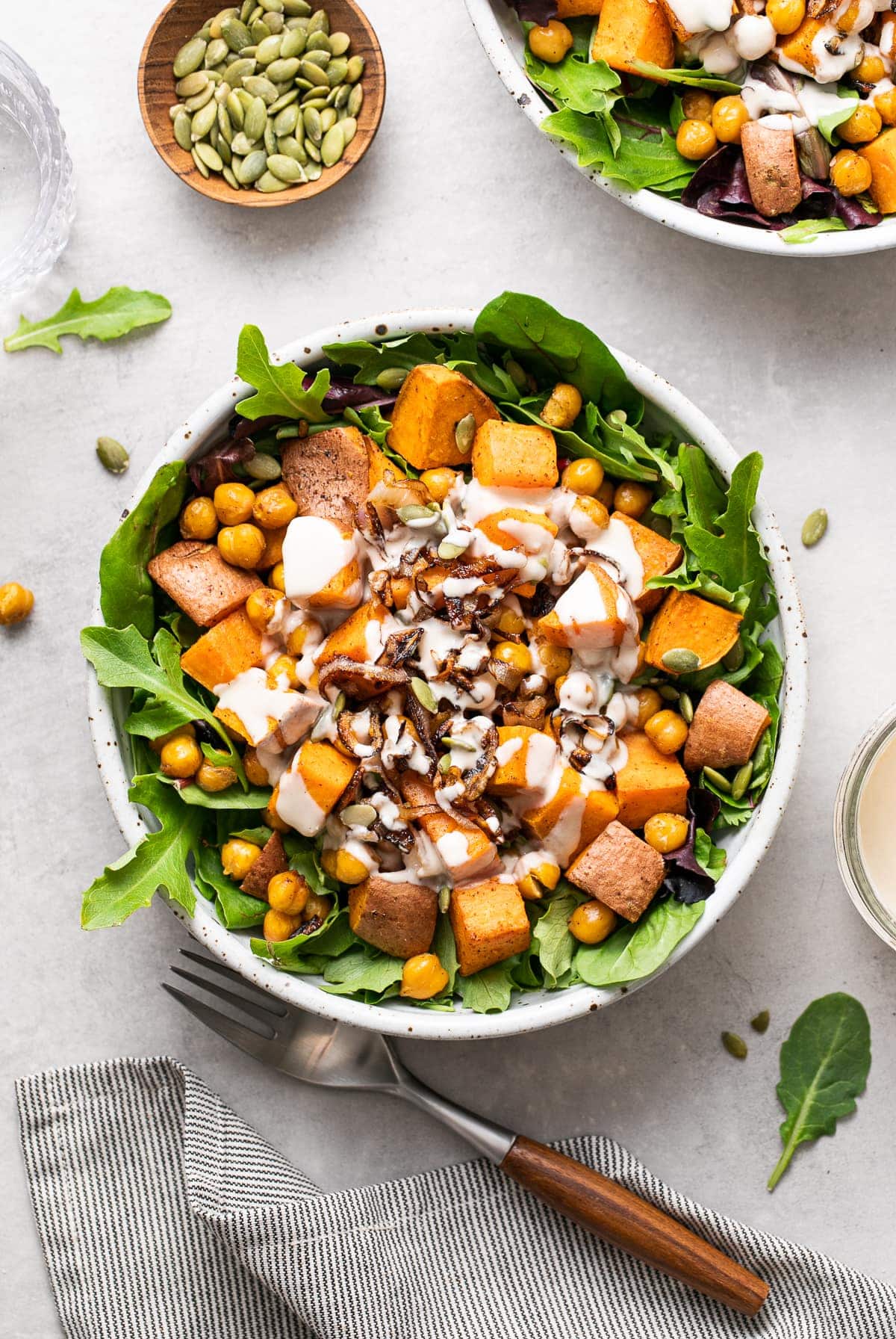 top down view of sweet potato chickpea salad with crispy shallots and tahini dressing with items surrounding.