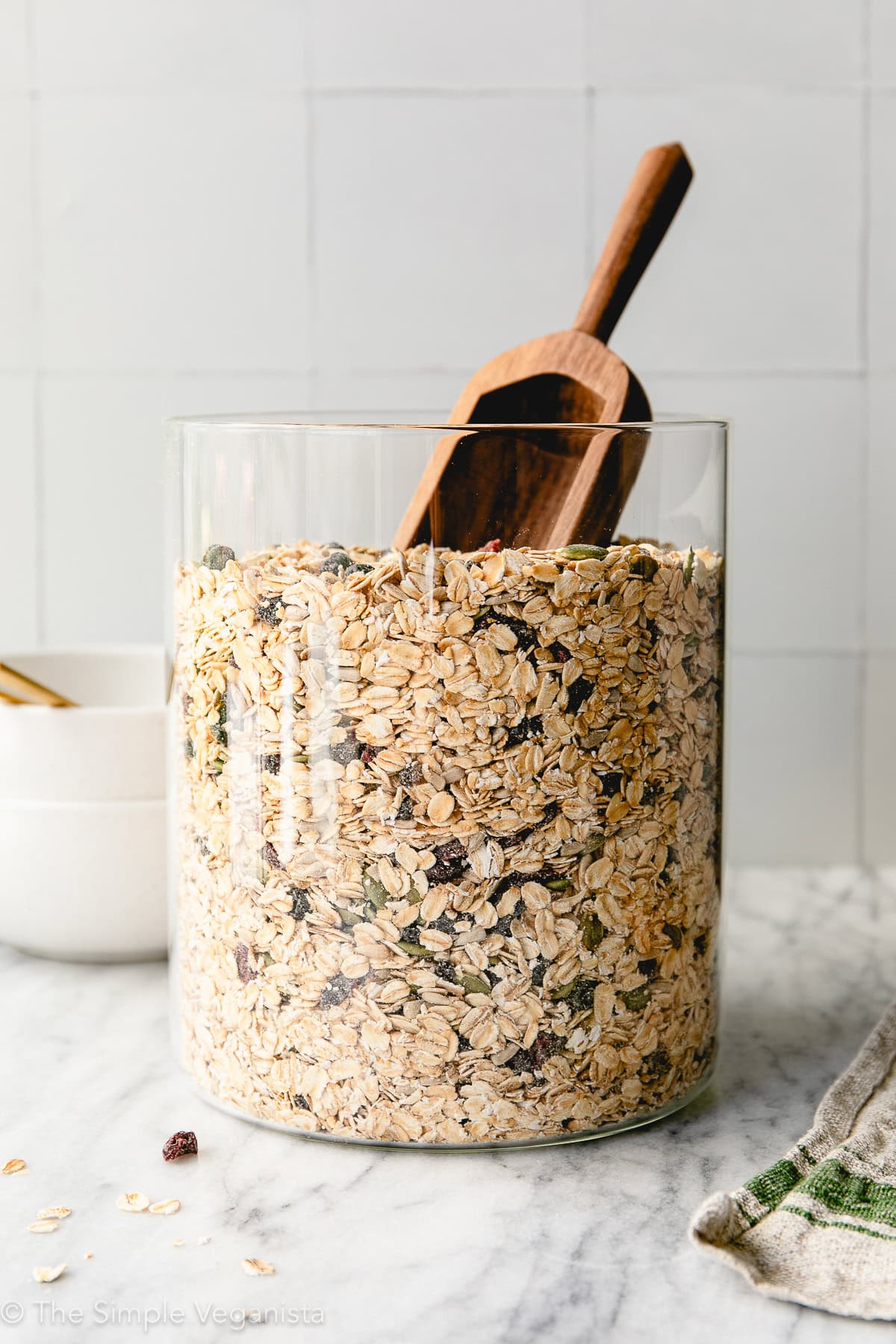 head on view of DIY muesli in a glass jar with wooden scoop and items surrounding.