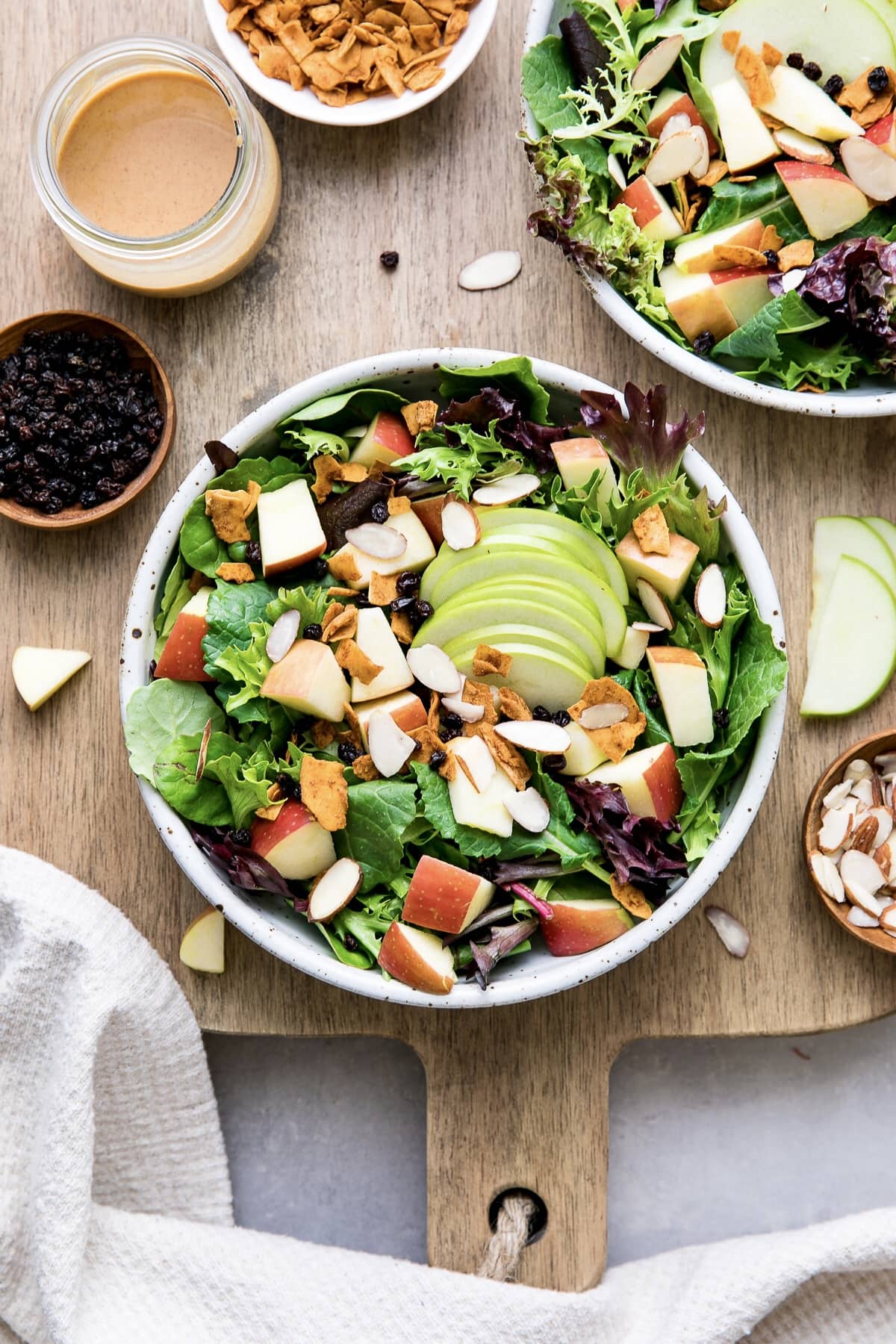 top down view of apple coconut bacon salad in a bowl with items surrounding.