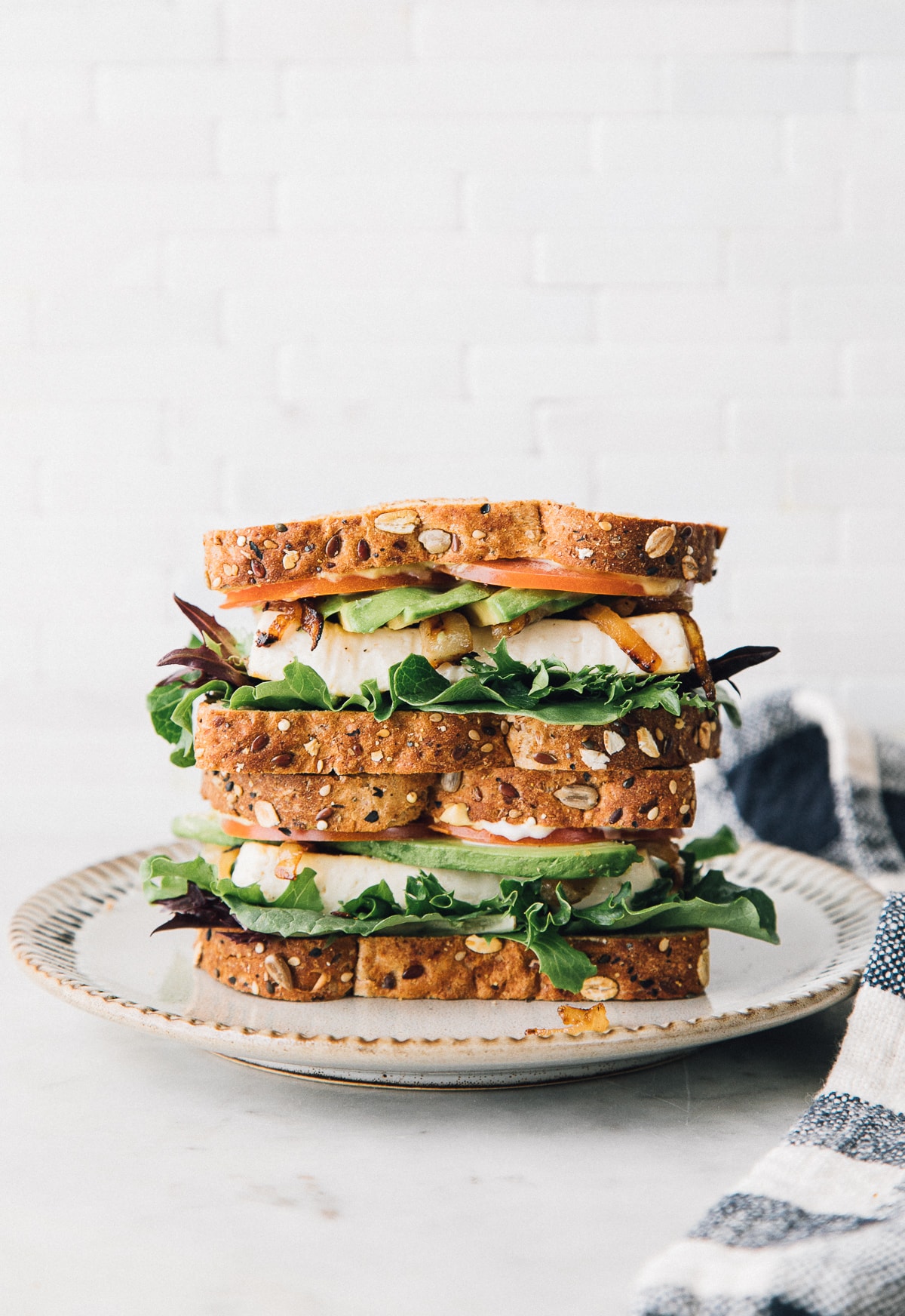 head on view of tofu avocado sandwich sliced in half and stacked on a small plate.