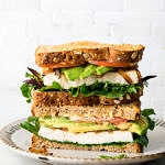 head on view of tofu avocado sandwich sliced in half and stacked on a small plate.