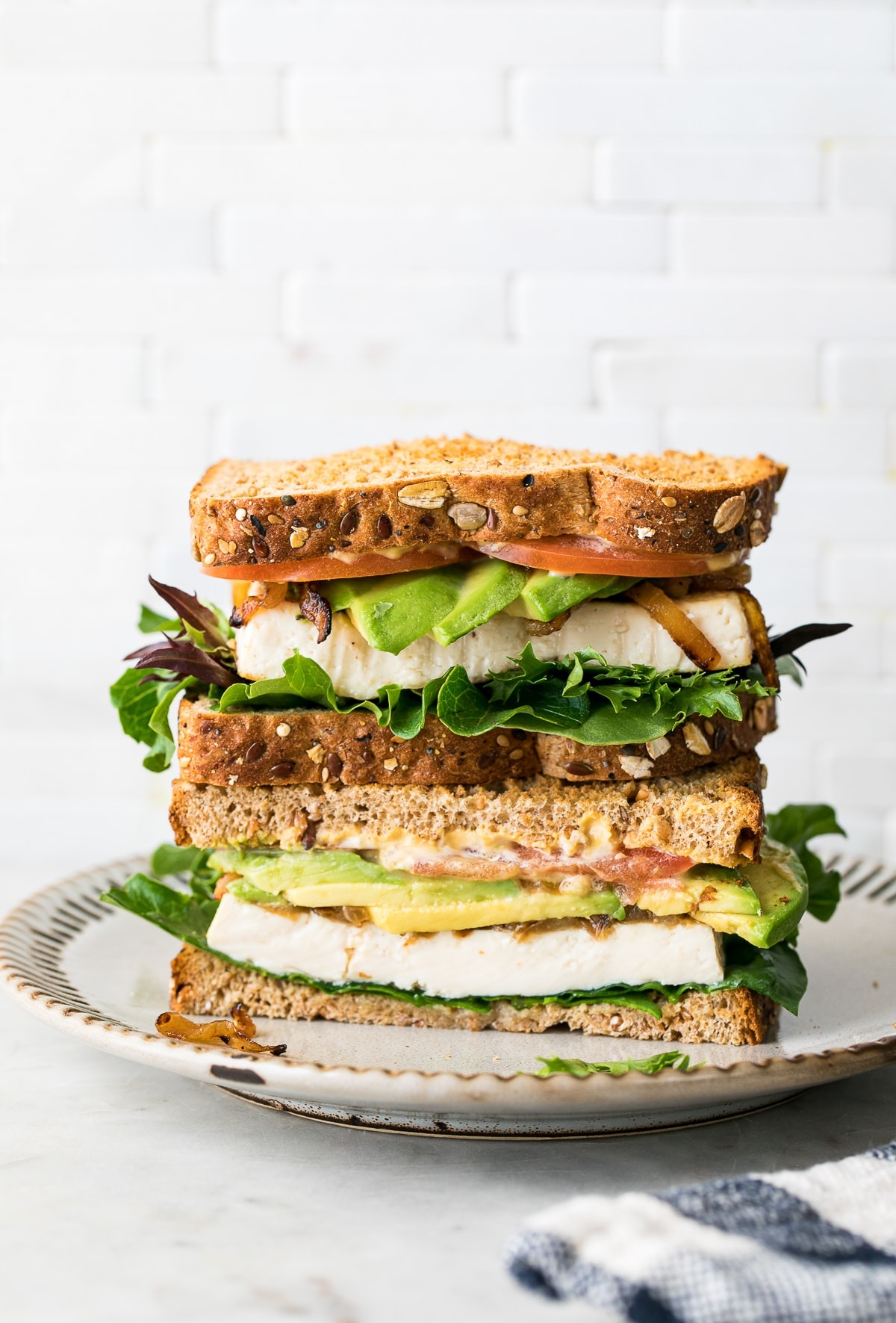 head on view of tofu avocado sandwich sliced in half and stacked on a small plate.