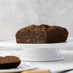 head on view of gluten free buckwheat banana bread on a cake stand with items surrounding.