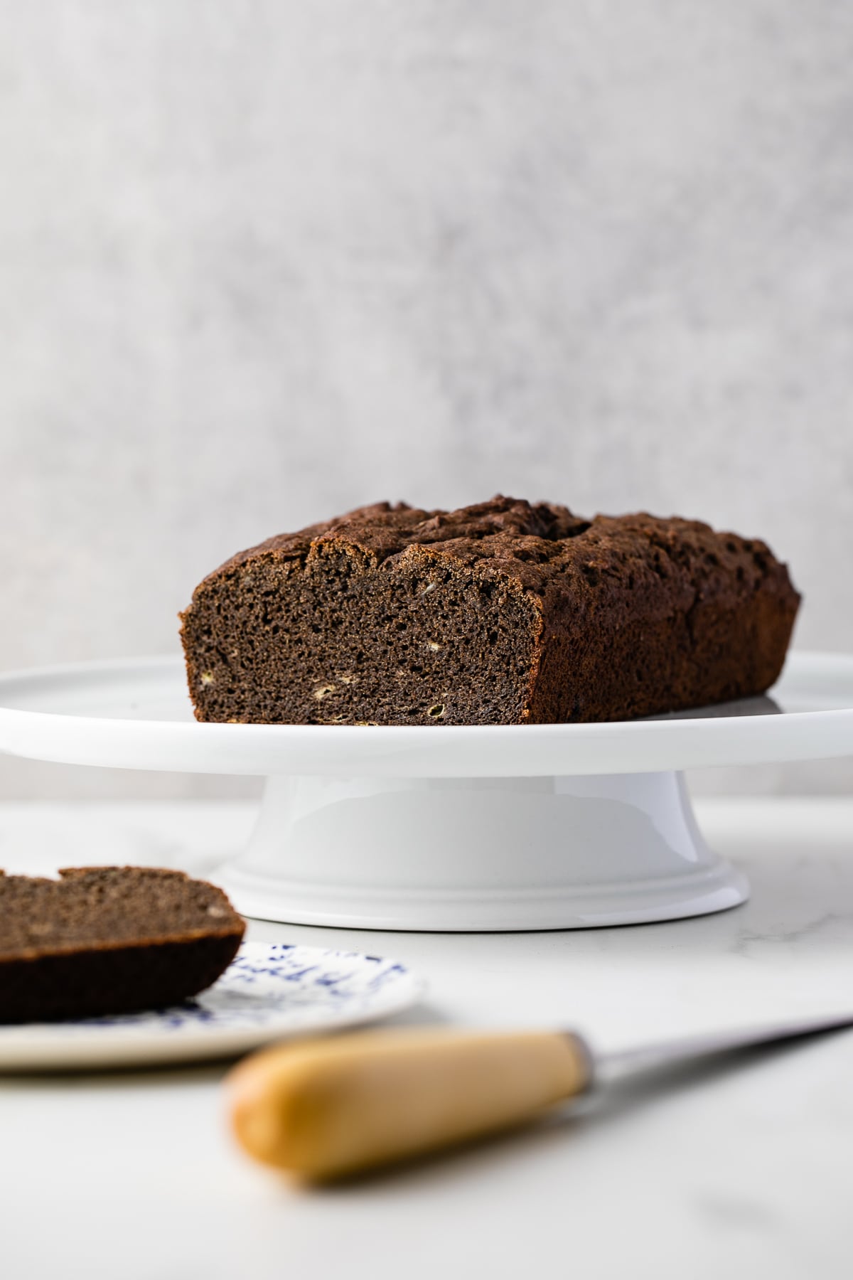 head on view of gluten free buckwheat banana bread on a cake stand with items surrounding.